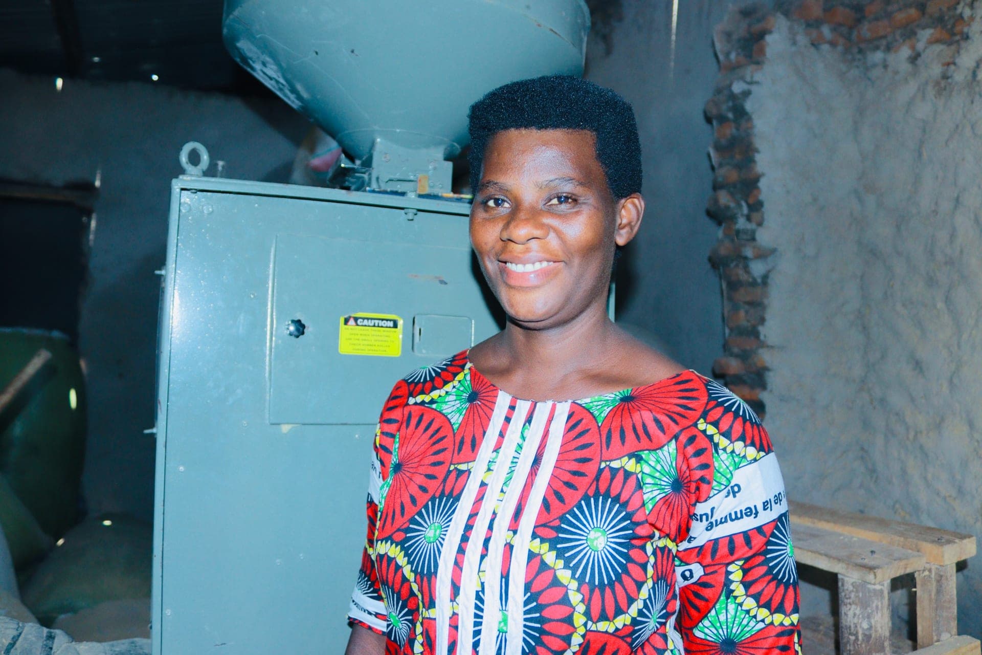 Woman entrepreneur smiling beside her grain milling machine